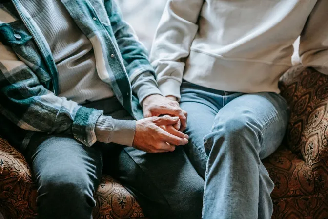 Two people sitting beside each other on a sofa, holding hands.