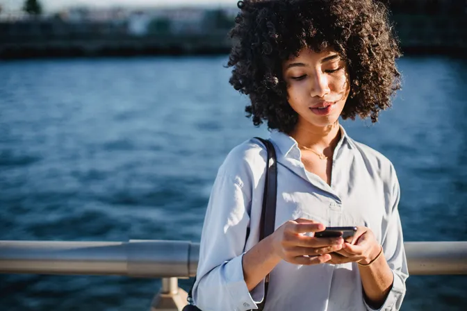 Woman with curly hair looking at her phone beside a waterfront.